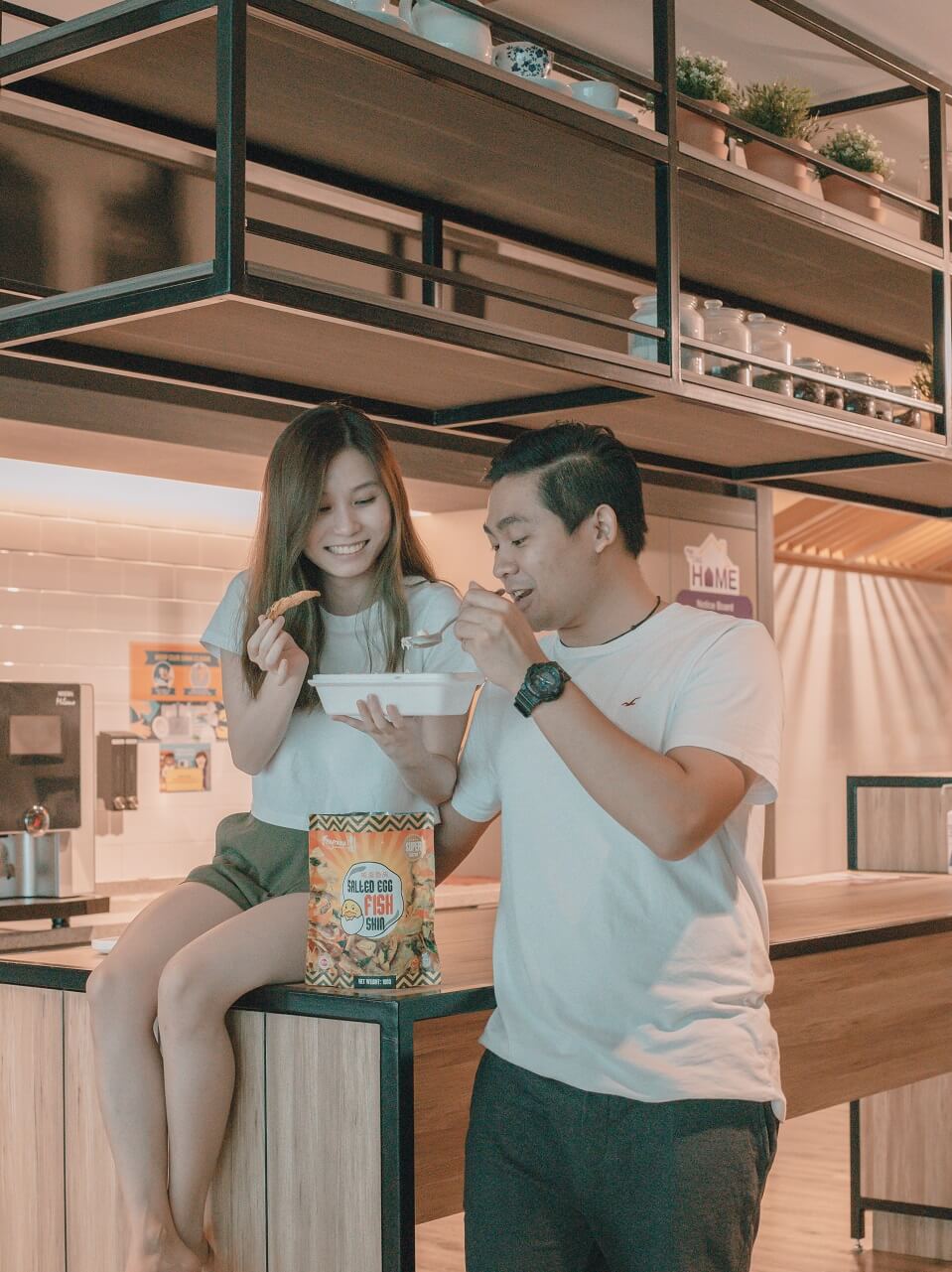A man and woman enjoying some snacks in a kitchen setting.
